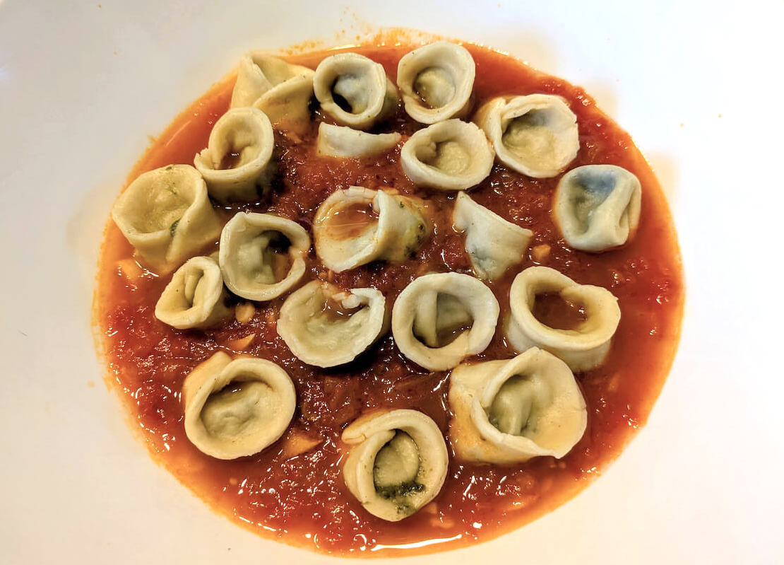 Tortellini served in a soupy sauce.